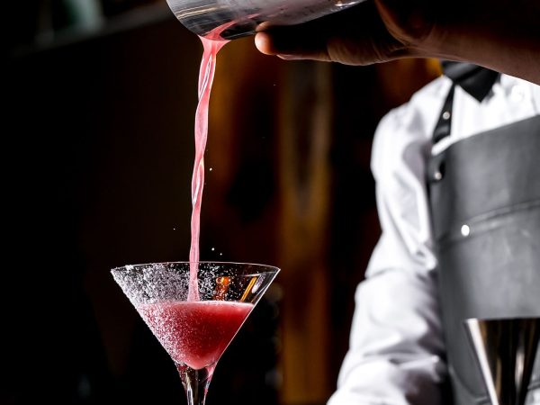 bar tender pours cocktail from cocktail shaker into martini glass